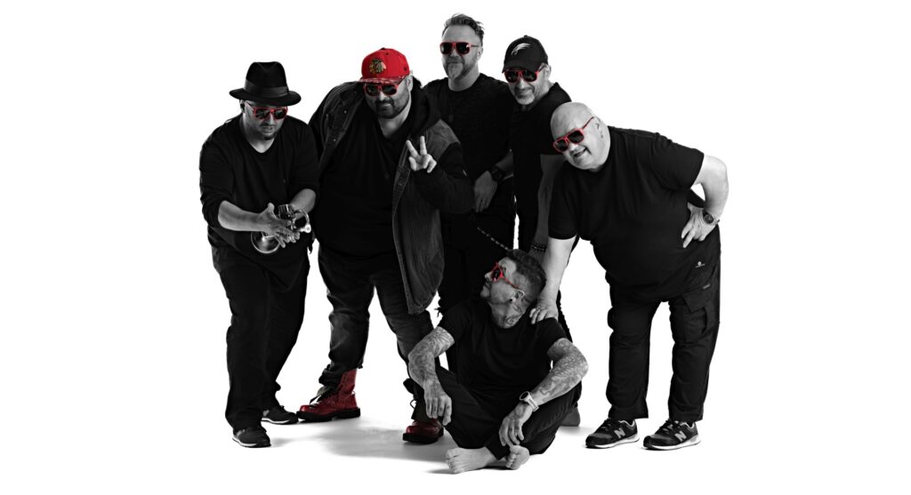Przedstawia sześciu facetów w czerni z motywami czerwonymi. Zespół muzyczny Piersi.