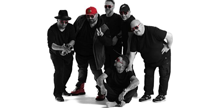 Przedstawia sześciu facetów w czerni z motywami czerwonymi. Zespół muzyczny Piersi.
