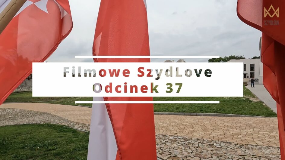 Plac z trawą i chodnikiem, bydynki w oddali, flagi biało-czerwone i napis Filmowe SzydLove Odcinek 37
